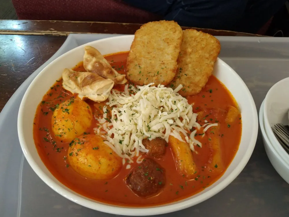 Bowl of tteokbokki with crispy hash browns, cheese and boiled eggs