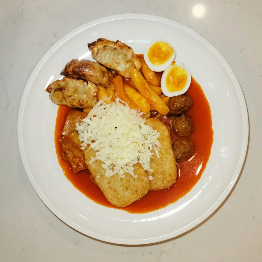 Tteokbokki plate with dumplings, hash browns, boiled egg and beef meatballs under melted cheese